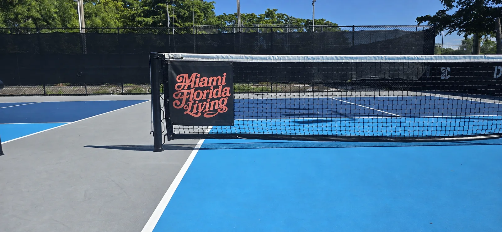 A 2 by 2 foot Miami Florida Living banner mounted at the post of a Dink Club court net, close up