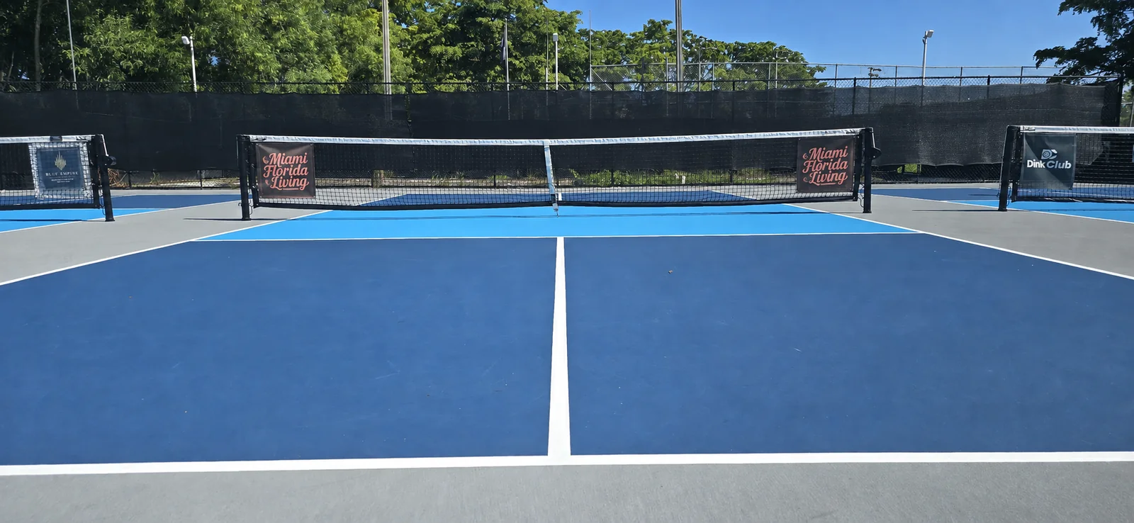 Full court view of two Miami Florida Living net banners on one net at Dink Club, with neighboring courts behind